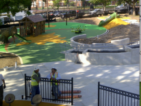Photo fo playground construction with play equipment partially installed.  Two construction workers can be seen working on the site.