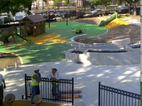 Photo fo playground construction with play equipment partially installed. Two construction workers can be seen working on the site.